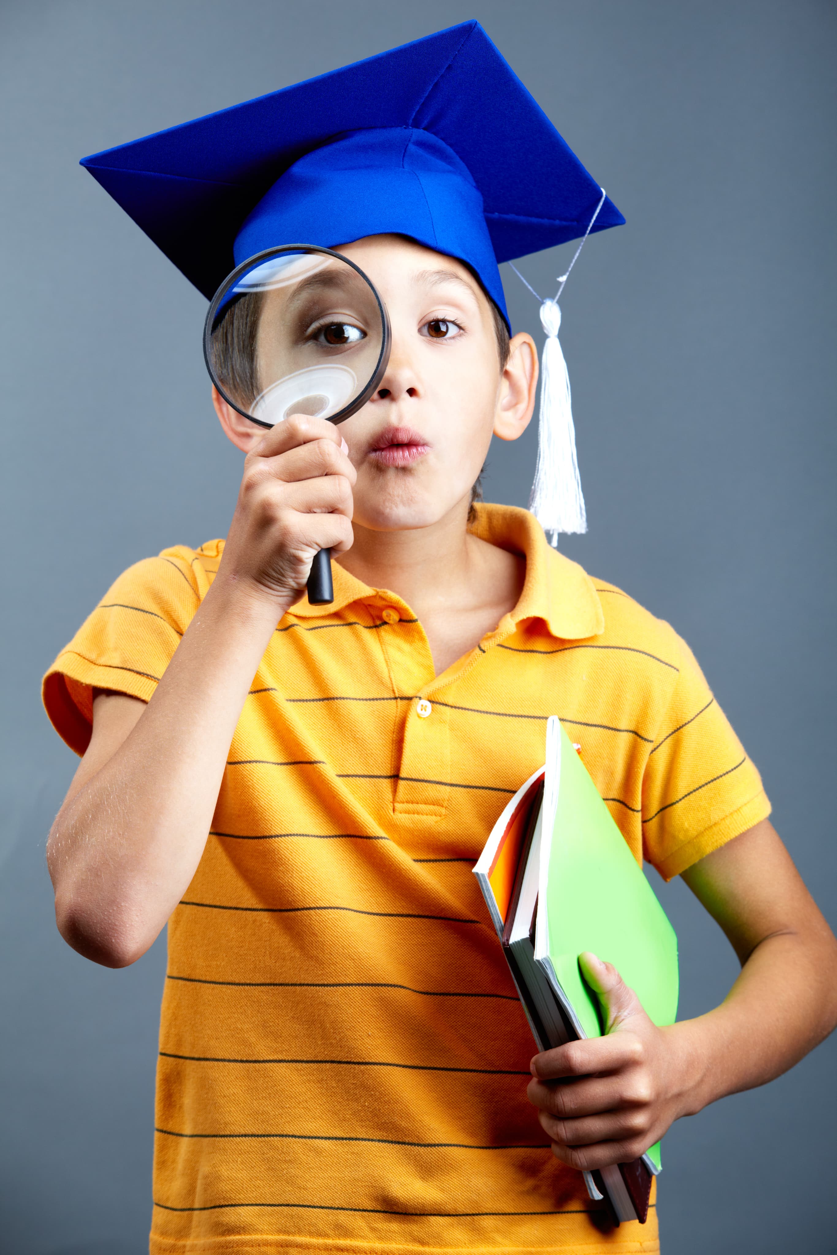 Child in a graduation cap holding a magnifying glass