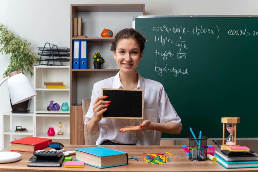 A teacher holding up a small slate at her desk